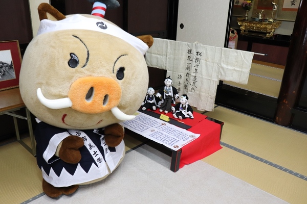 衣装を着たまるいのが畳の部屋で机の前で座っている写真