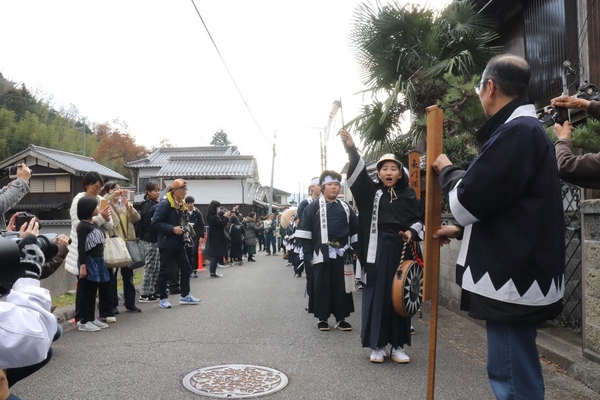 列をつくり衣装を着た子どもたちが手を挙げながら歩く様子と、見守る観客