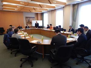 円形の会議机に着席して各々資料に目を通す委員たちの写真