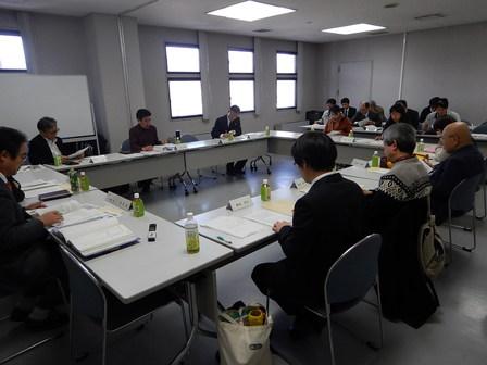 ホワイトボードのある会議室で各々着席して会議を行う委員たちの写真