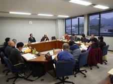 夕闇の空が窓の外に見える会議室で集まる委員たちの写真