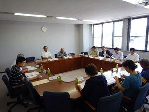 窓から陽が差し込む会議室で着席し会議を行う委員たちの写真