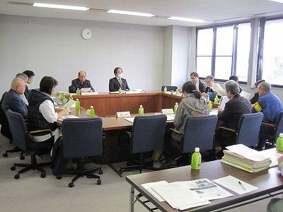 会議室内で資料を手に持ち、会議を行う委員たちの写真