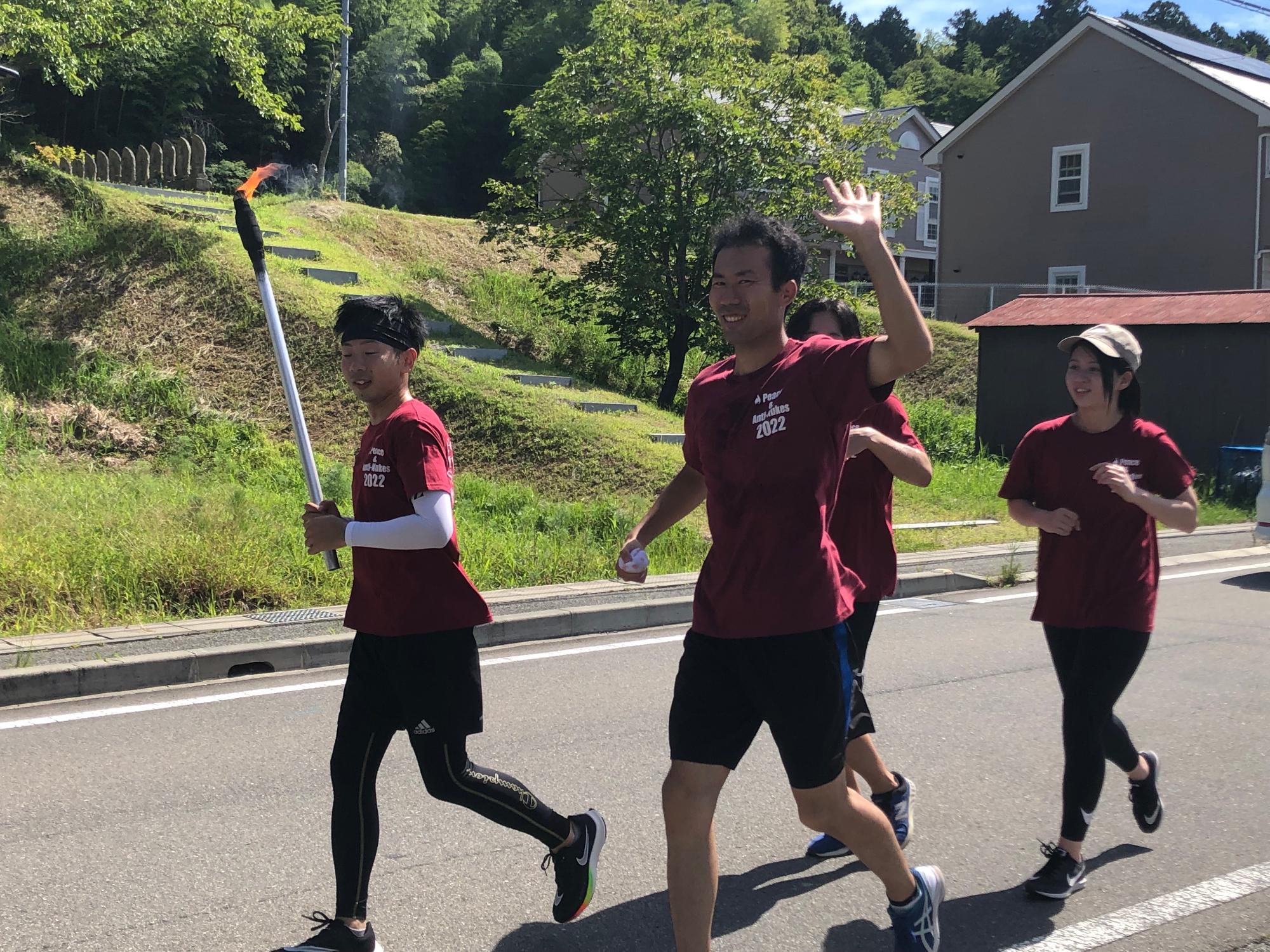 トーチを持った男性と、3名のランナーが走っている