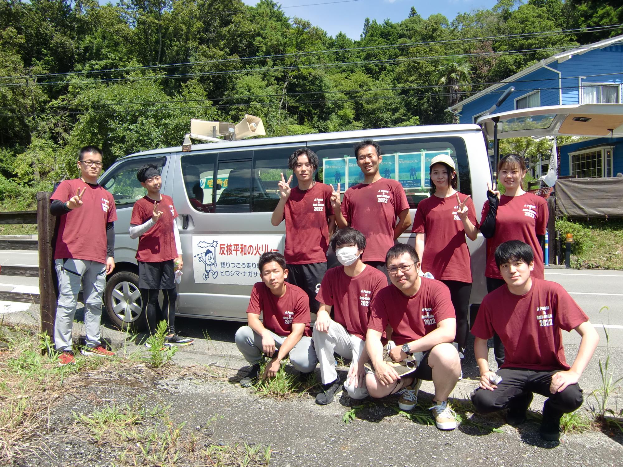 箱バンの前に、おそろいの赤いシャツを着たランナーとスタッフの記念撮影