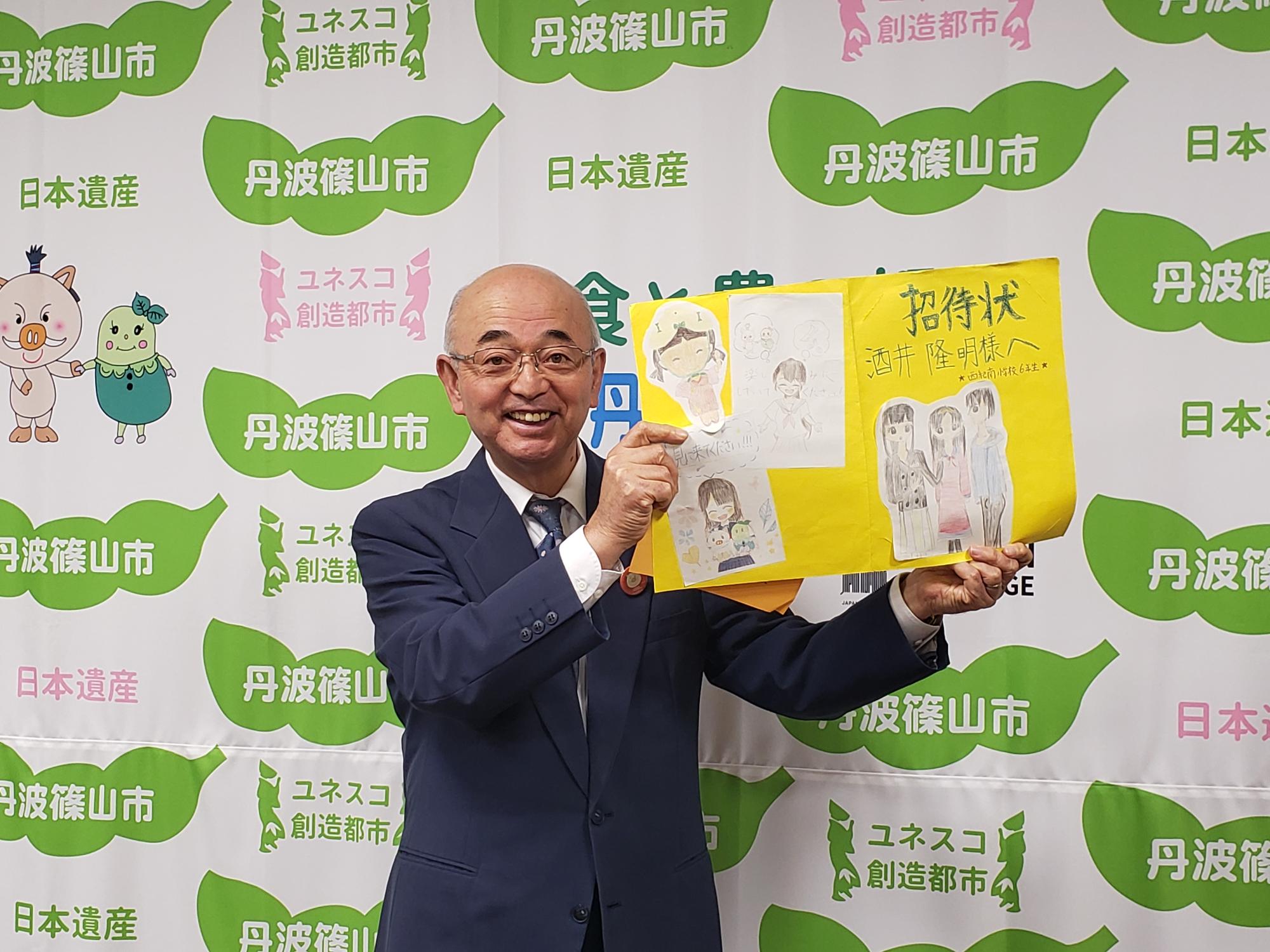 子ども達からもらった手書きの招待状を手にしている市長