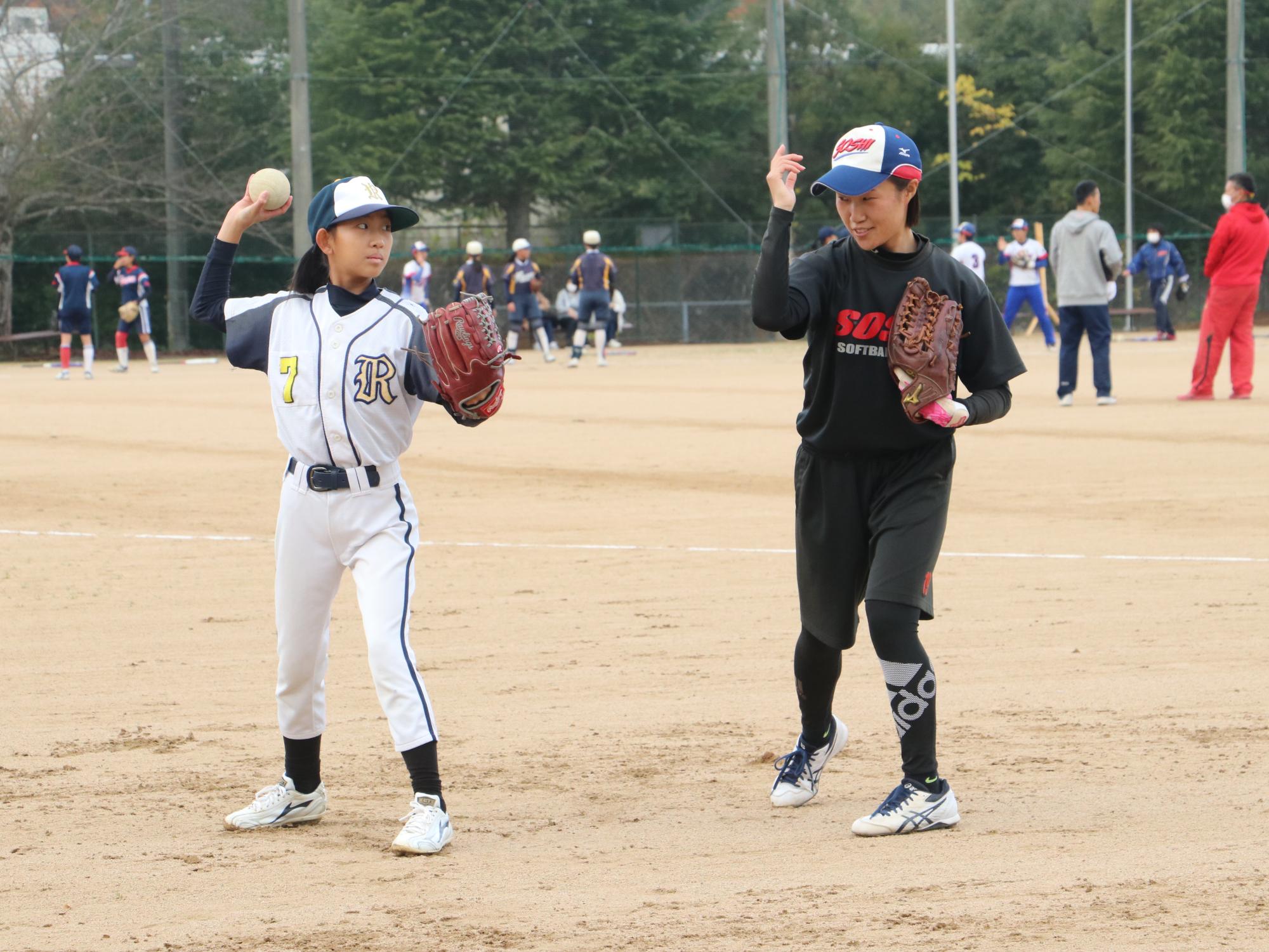 ソフトボールの交流試合で高校生が投げ方を指導している