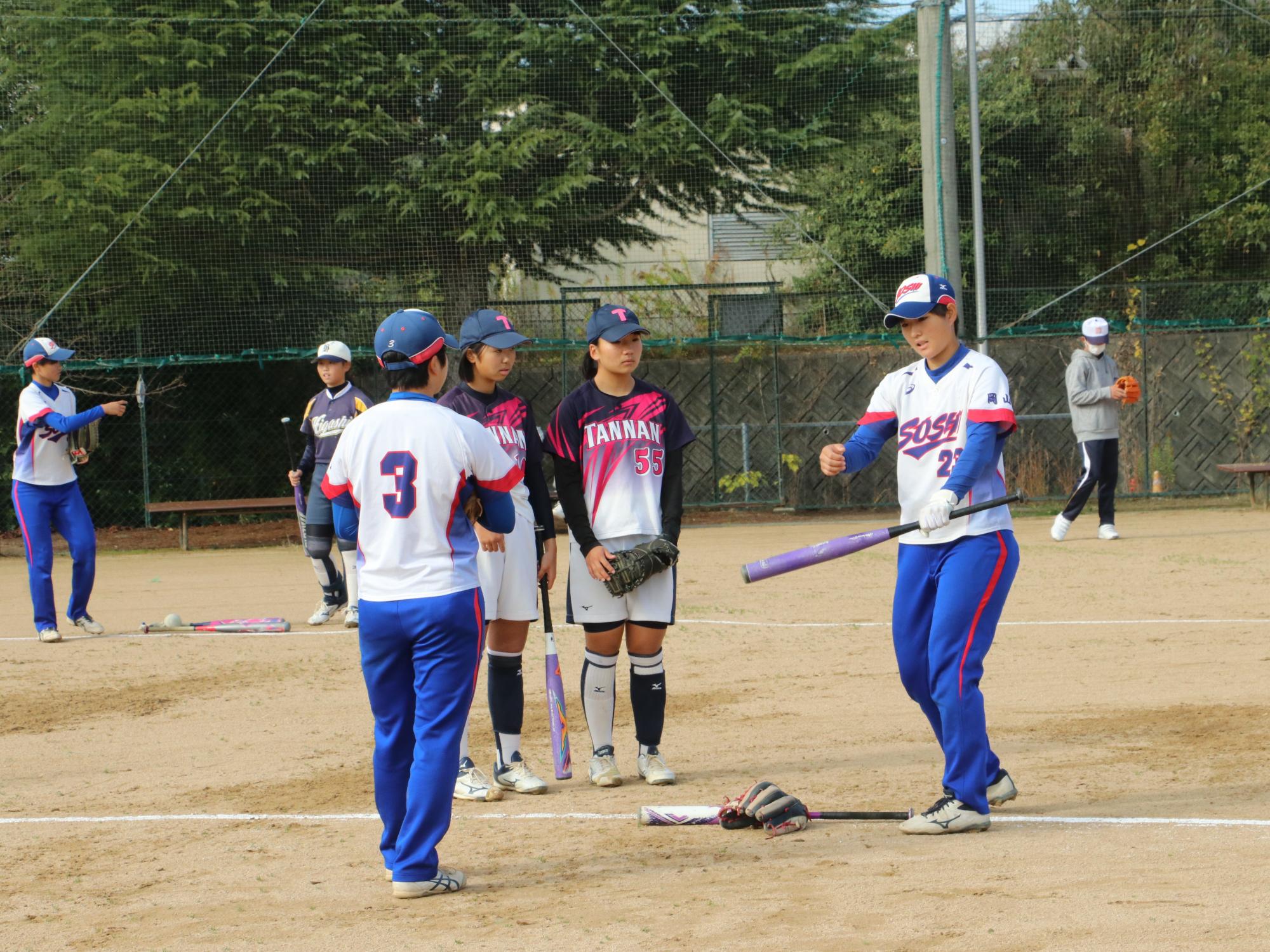 ソフトボールの交流試合で高校生がバッティングの指導をしている
