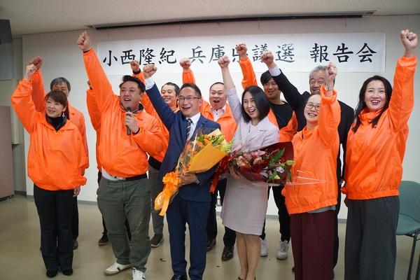 小西 たかのりさんが当選され花束を手に取り「エイエイオー!」を仲間達と一緒にしている写真