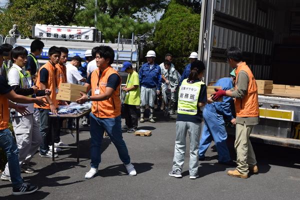 総務班と書かれたゼッケンを着ている人たちがトラックから荷物を降ろしている写真