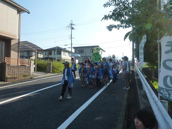 まめりんの神輿を担いだ子供らが沿道を歩いている写真