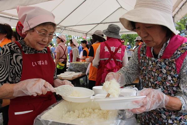 テントの中でエプロンをつけた女性二人がご飯を紙皿によそっている写真