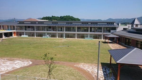 中央には緑の芝生があり、奥には2階建てで壁が透明のガラスになっている横長の建物が映っている写真