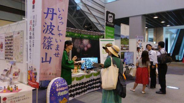 緑の法被を着た女性が丹波篠山の商品を宣伝しており、麦わら帽子を被った2名の方が話を聞いている写真