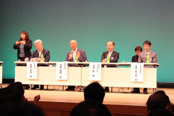 パネリストで参加された男性4名の方々が座っており、マイクを持ち市長が話をしている。その話の内容を手話で示している女性の方の写真