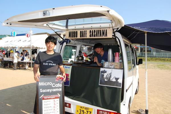 カフェの車内販売の前でメニューを持っている男性と車内にいる男性が記念撮影している写真