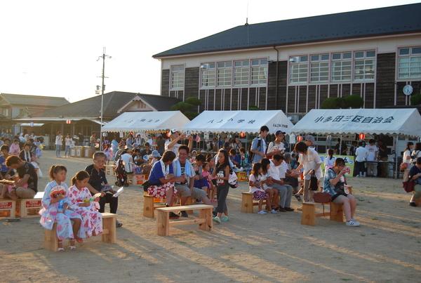 校舎の前にテントが張られ、校庭に設置されている椅子に座ってくつろぐ人々の写真