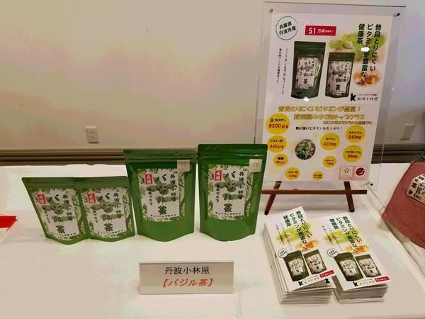 パックに袋詰めされた健康茶がパンフレットやパネルと一緒にテーブルに展示されている写真