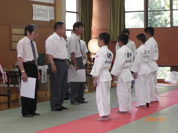 柔道着姿の4名の少年の前に3名の表彰状を持った男性達が立っている写真