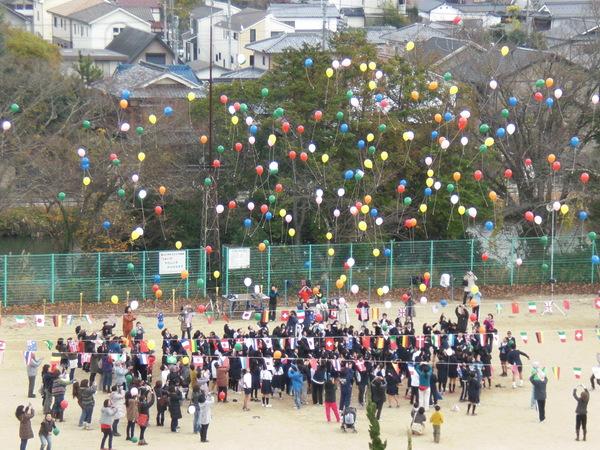 生徒たちの手から離れて、空高く飛ぶ色とりどりの風船とそれを眺めている生徒の写真
