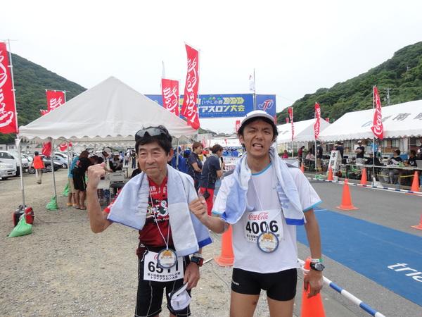 山田 幸広さんと安福 直剛さんが手作りのメダルを首にかけ2人でガッツポーズしている写真