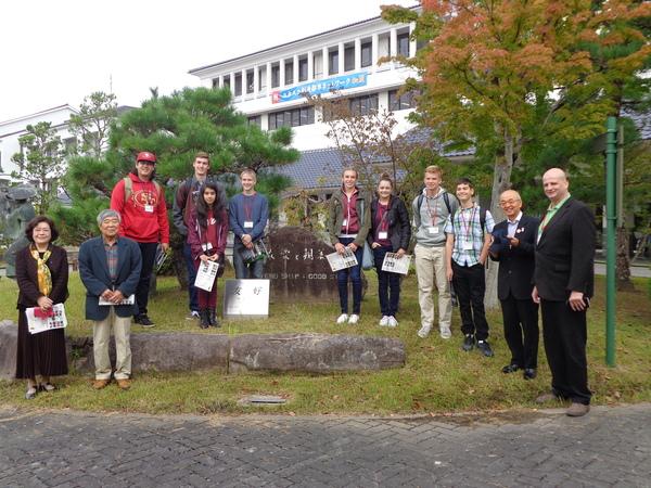 石碑の周りに並ぶ外国人男女と、市長、関係者の集合写真
