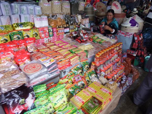 たくさんのお菓子が敷き詰められて、そこに女性が椅子に座り店番している写真