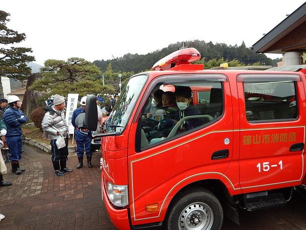 消防車に子供達が3人乗って車の中や外を見ている写真
