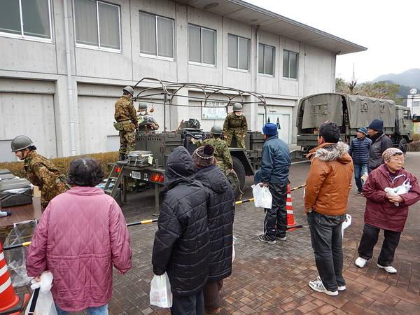 自衛隊が車の荷台から荷物を降ろしている所を地域の方が見ている写真