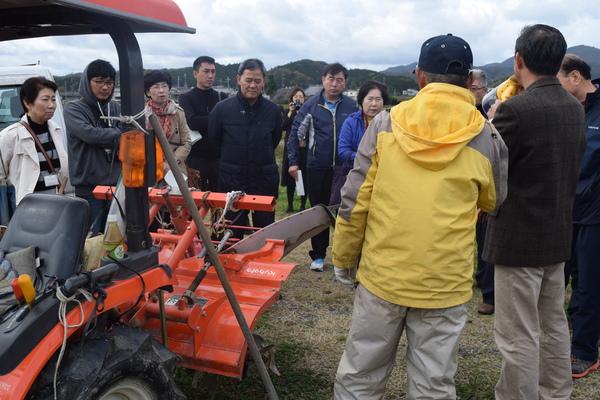 トラクターの横でスピーカーで話をしているのを聞いている人々の写真