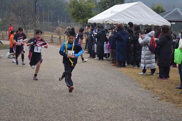 襷をもらった男子と女子が走り出したのを父兄が応援してる写真