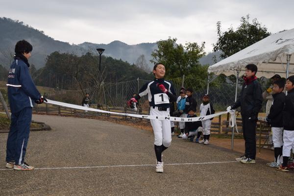 野球部ユニホームを着た生徒がゴールテープを切る写真