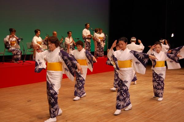 白地に笹の葉の模様が絵が描かれている着物を着た踊り子たちが三味線や尺八などの演奏に合わせて踊りを踊っている様子の写真