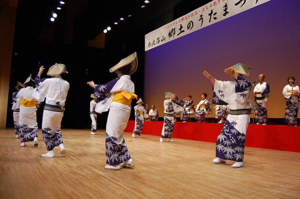 編み笠をかぶり、白地に笹の葉の模様が絵が描かれている着物を着た踊り子たちが三味線や尺八などの演奏に合わせてデカンショを踊っている様子の写真