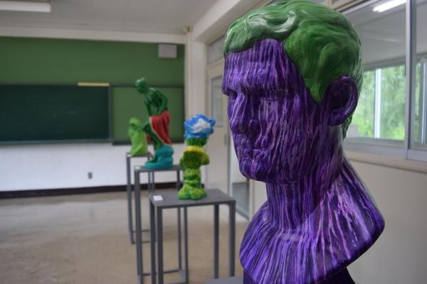 紫の顔に緑の頭の人間のオブジェが飾られている写真