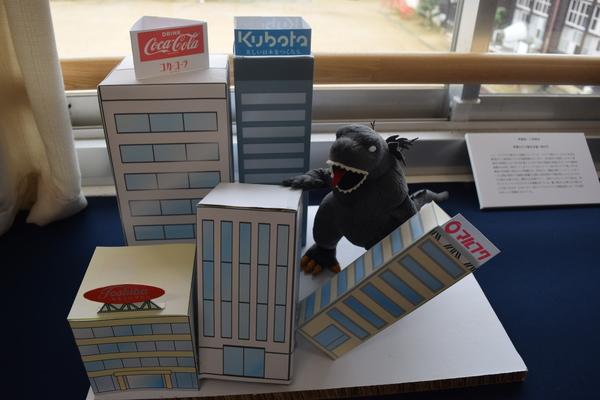 紙で作られたビルを作り物の恐竜が倒している作品が飾られている写真