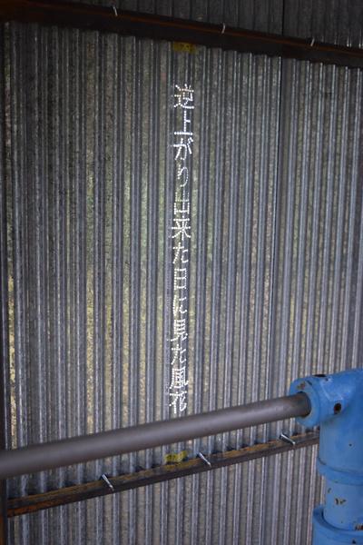 トタンの壁に「逆上がり出来た日に見た風花」と白い文字で書かれている作品の写真