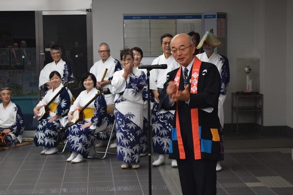 市長がスタンドマイクの前で話をしており、後ろの方にはデカンショの演奏をする演奏者と踊り子の皆さんが写っている写真