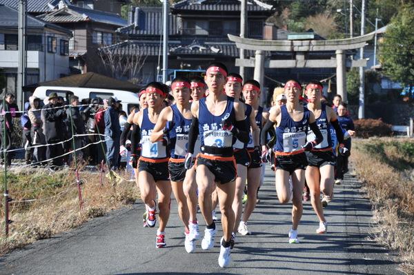 鉢巻きにユニホーム姿の西脇工業高校男子陸上部の選手らが鳥居を通過した辺りを走っている様子を見ている人々の写真