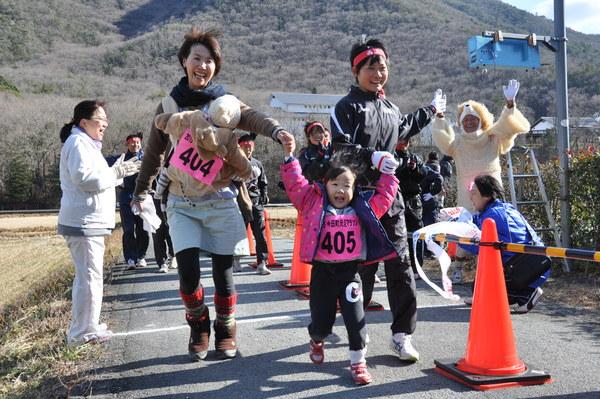 子供を抱っこ紐で結んだ母親と西脇工業高校女子陸上部の生徒が女の子の手を握ってゴールしている写真