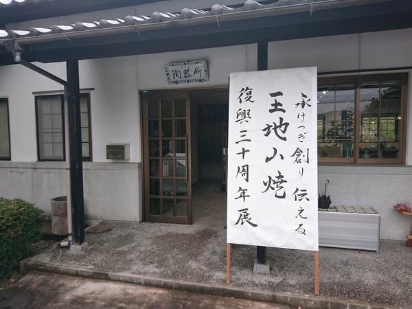 陶器所の入り口に「承けつぎ創り伝える 王地山焼 復興陶器所三十周年展」と書かれた看板の写真