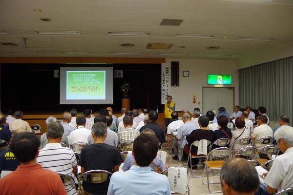 30名ほどの人たちが座っている前で男性がマイクを持って話している写真