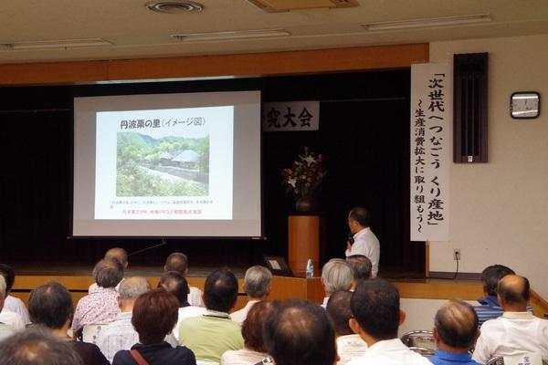 丹波栗の里と書かれたスクリーンが前にありその横で男性が説明をしている写真