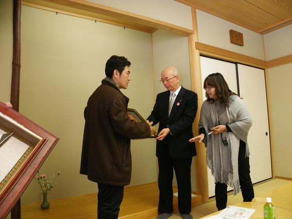 団長の黄 肇崇(こう ちょうすう)さんが市長に額に入った絵画のような物を手渡しており、グレーのストールを羽織った女性が市長に説明をしている様子の写真