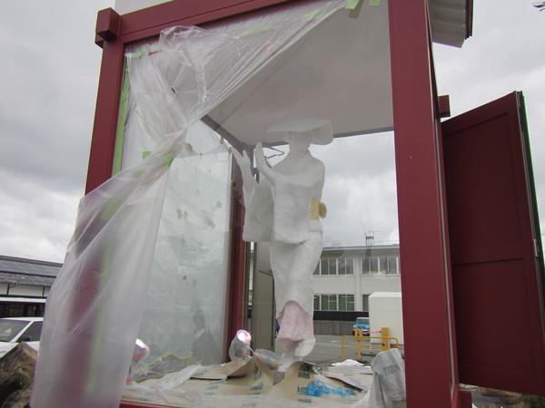 着物をきた人が手をたたこうとしているデカンショ人形と人形を入れる建設中の木の枠を朱色にぬられたケースの写真