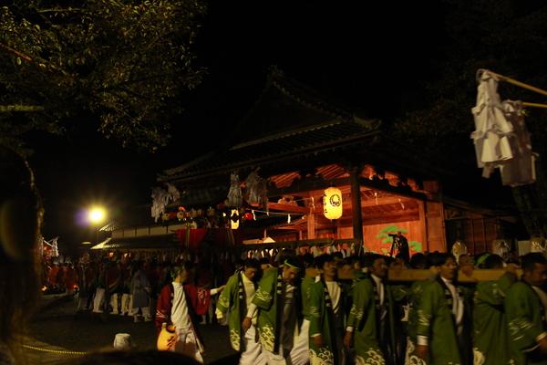 提灯に灯りがともっている神輿を法被姿の男性らが担ぎ練り歩いている写真
