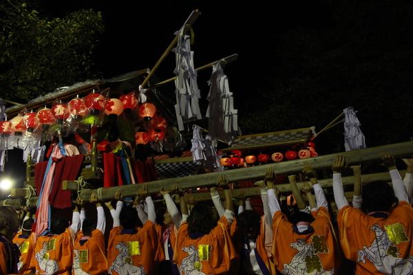 夜、法被姿の人々が神輿を持ち上げている写真