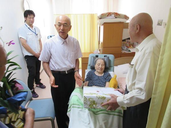 市長より、ベッドに座っているおばあちゃんにお祝い品を渡している写真