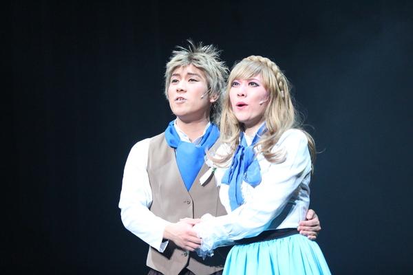 金髪の女性と男性が手を繋いで遠くを見て歌っている写真