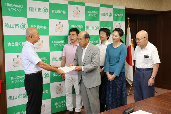 市長から書類を受けとる男性と、その後ろに並ぶ4名の男女の写真